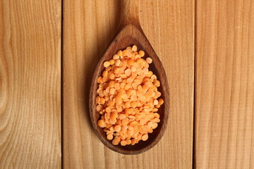 Red lentils on wooden spoon at plank background. Directly Above.