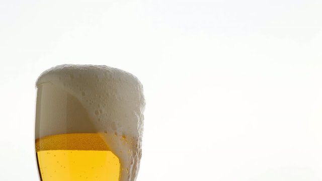 Close up glass of lager beer with bubbles and froth in glass, overfill and run out. foam flows down a glass of beer
