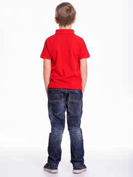 Full length portrait of a child standing back to the camera. Kid stands at studio.  Little boy dressed in red t-shirt and jeans, posing at studio, Back view