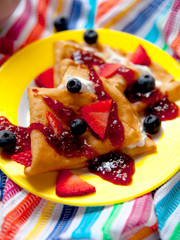 Close up of two thin pancakes, folded in triangles, are poured with sour cream, jam and decorated with fresh berries. The concept of Russian holiday Maslenitsa
