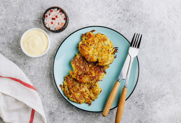 Homemade potato pancakes or hash brown on blue plate with sauce on gray table. Traditional dish in...