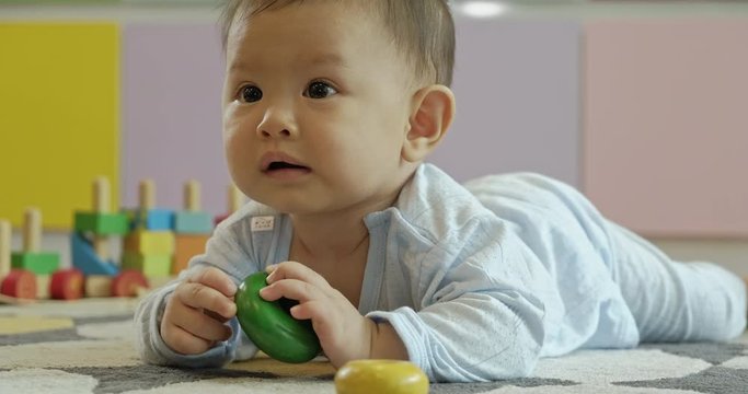 Asian baby crawing on floor in living room, Holding wooden toy. Childhood and nursery service concept.