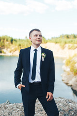 Groom stands on the lake background and smiles