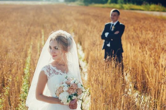 Young wedding couple standing in a field of pigweed in the setting sun. Newlyweds hug with a smile.