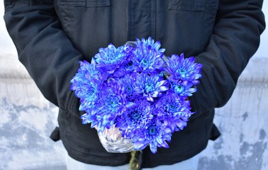 A man holds a bouquet of blue chrysanthemums