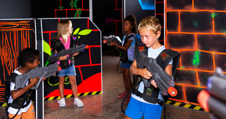 Group of glad pleasant teenagers with laser guns having fun on dark lasertag arena