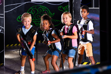 Cheerful teen girl and boys with laser pistols posing together in dark laser tag labyrinth
