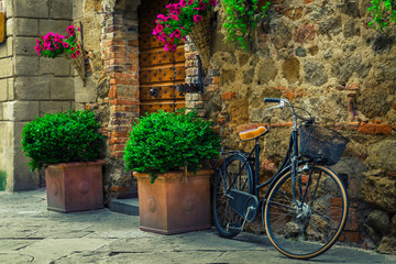 Fototapeta na wymiar Cute street with flowery entrance and retro bicycle, Pienza, Tuscany