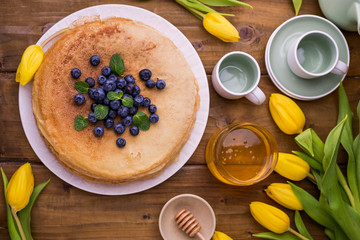 Large traditional Russian pancakes with berries and honey on a wooden table. Baking for the spring holiday Shrovetide and a bouquet of yellow tulips. Copy space