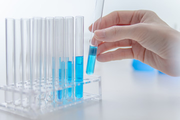 Hand of scientist pick up test tube that contained blue chemicals from rack in the laboratory.