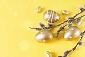 Golden colored Easter eggs and spring tree branches over yellow background. Happy Easter time.