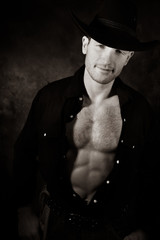 Portrait of handsome cowboy looking at camera with open black shirt revealing muscular pecs and...