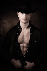 Portrait of handsome cowboy looking at camera wearing hat with open black shirt revealing defined...