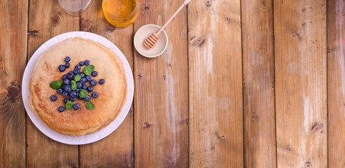 Pancakes with blueberries and honey on a plate, on wooden roofing. Traditional pastries for the Russian festival of Maslenitsa. free space for text.