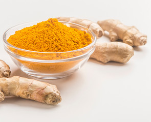Turmeric roots with turmeric powder in glass jar on white