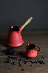 Ceramic cup, coffee cezve, coffee grains, wooden background and pieces of chocolate