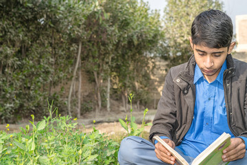 a young boy is reading book and sitting in the garden 