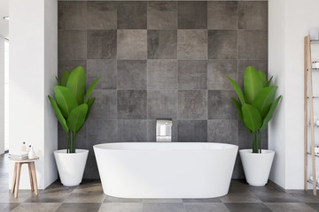 Bathtub and plants in tiled bathroom interior