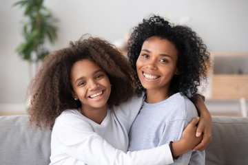 Happy african mother and teen daughter embracing looking at camera