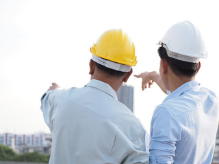 asian male engineer or foreman and architects asian people  wear safety helmet are pointing to highrise building.
