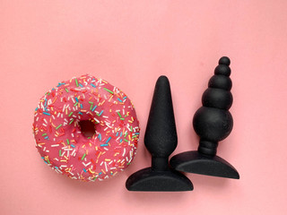 Sex toys. Pink donut and two black butt plags on a pink background. Useful for sex shop, adult