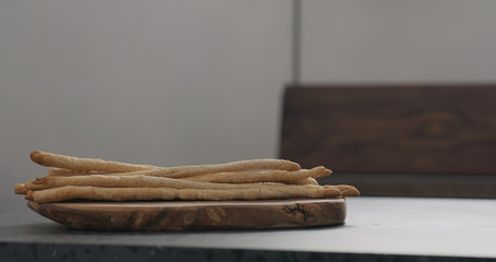 bunch of homemade grissini on olive board on concrete countertop