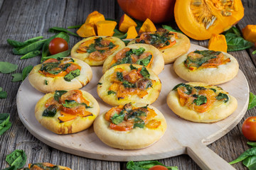 Mini pizzas with pumpkin, spinach and tomatoes on a pizza shovel