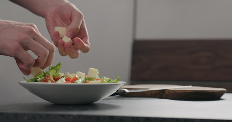 man adding cheese to make salad in white bowl