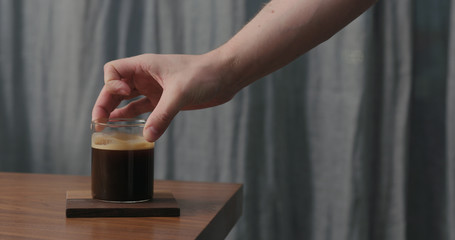 man hand put glass with coffee on walnut table