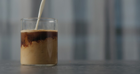 cream pour into coffee in glass on concrete countertop