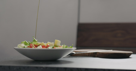 adding olive oil to make salad in white bowl