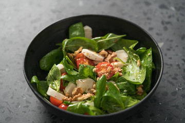 Salad with spinach, tomatoes and mozzarella in black bowl on concrete countertop