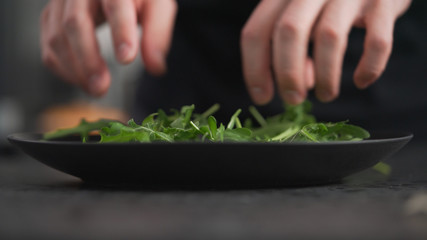 man hands arranging fresh arugula on black plate