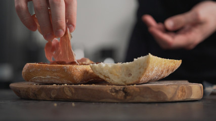man add prosciutto on ciabatta on olive board
