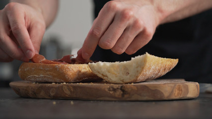 man add prosciutto on ciabatta on olive board