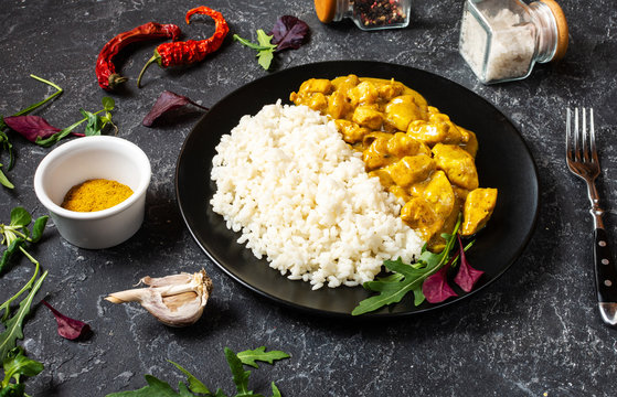 Rice with chicken in curry sauce on plate on black stone background