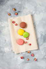 Different types of macaroons and pink flowers on concrete background. Top view.