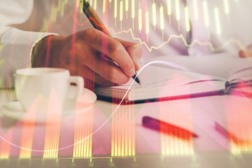 Double exposure of man's hands writing notes of stock market with forex chart.