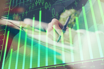 Financial forex graph displayed on hands taking notes background. Concept of research. Multi...