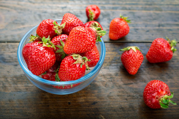 Ripe strawberries in a glass bowl on a wooden table.