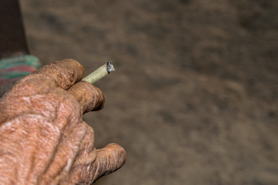 man is smoking homemade tobacco leave made cigarette and wrinkles on his hand