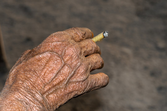 man is smoking homemade tobacco leave made cigarette and wrinkles on his hand