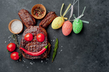 Grilled festive Easter steak with spices and colorful eggs. Easter bunny on stone background with copy space for your text.
