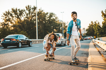 Beautiful young couple enjoying skateboarding on city street.