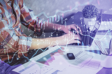 Double exposure of stock graph with businessman typing on computer in office on background. Concept of hard work.
