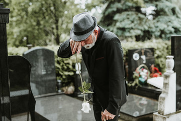 Elegant sad elderly man grieves at the grave of a loved person