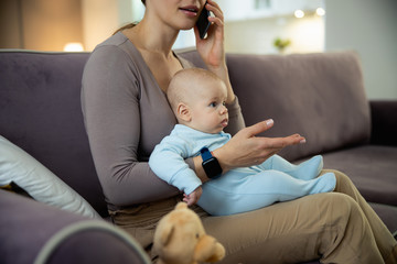 Smiling young mom sitting with baby and using smartphone