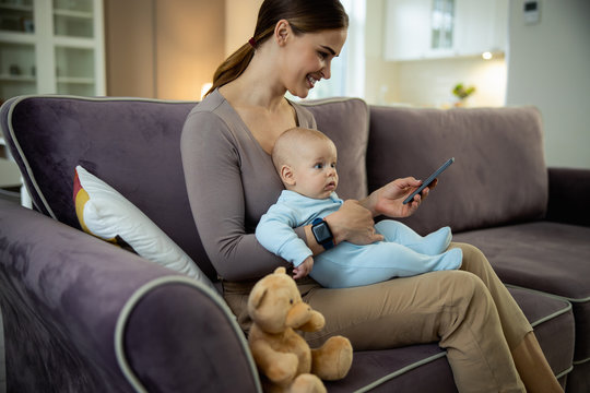 Smiling young mom sitting with baby and holding smartphone