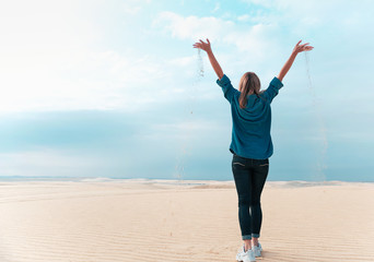 Obraz premium Happy woman in desert with raised hands full of sand, copy space.