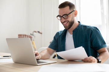 Happy young businessman in eyeglasses working on computer.